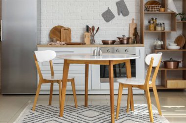 Mutfağın içinde beyaz tezgahlar, buzdolabı ve yemek masası var.