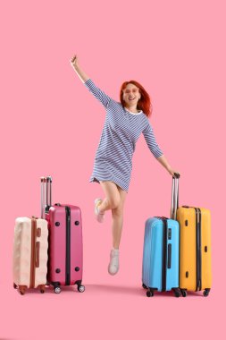 Pembe arka planda bir sürü bavulu olan zıplayan kadın turist.