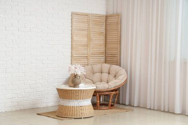 Beyaz tuğla duvarın yanındaki sehpada güzel orkide çiçekleri olan rahat bir koltuk ve vazo.