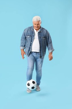 Olgun adam mavi arka planda futbol topuyla oynuyor.