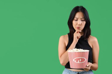 Yeşil arka planda patlamış mısırı olan düşünceli genç, güzel Asyalı kadın.