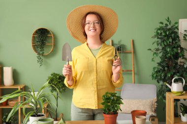 Saf şapkalı, elinde makasla ve yeşil odasındaki bahçe malasıyla mutlu bir kadın.