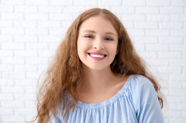 Beyaz tuğla duvarın yanındaki mutlu kızıl saçlı kadının portresi.