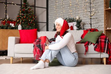 Genç bir kadın Noel arifesinde sıcak kakao içiyor.