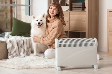 Samoyed köpekli genç bir kadın radyatörün yanında ısınıyor.