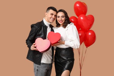 Kalp şeklinde balonları ve kahverengi arka planda hediye kutuları olan sevgi dolu genç bir çift. Sevgililer Günü 'nün kutlaması