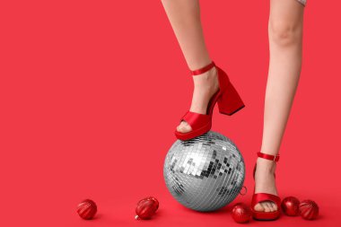 Disko topu ve kırmızı arka planda Noel dekoru olan yüksek topuklu kadın bacakları.