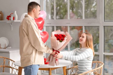 Sevgililer Günü 'nü evde, mutfakta gül buketiyle kutlayan güzel genç bir çift.
