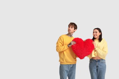 Beyaz arka planda kalp şeklinde yastığı olan genç bir çift. Sevgililer Günü kutlaması