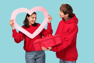 Mavi arka planda Sevgililer Günü hediyesi ve kalp şeklinde çerçeveli genç bir çift.