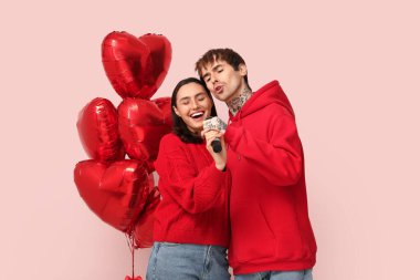 Pembe arka planda kalp şeklinde balonları olan şarkı söyleyen genç bir çift. Sevgililer Günü kutlaması