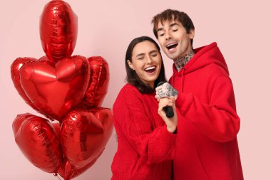 Pembe arka planda kalp şeklinde balonları olan şarkı söyleyen genç bir çift. Sevgililer Günü kutlaması