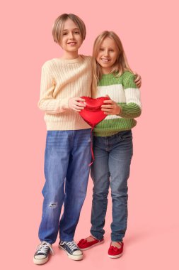 Kalp şeklinde balonları olan küçük çocuklar pembe arka planda sarılıyorlar. Sevgililer Günü kutlaması