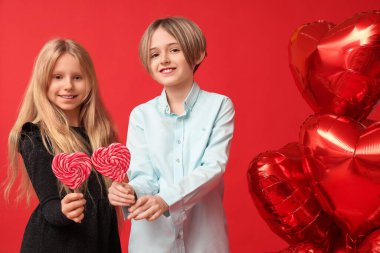 Little children with lollipops and heart-shaped balloons on red background. Valentine's Day celebration