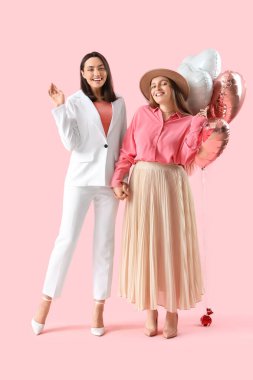 Pembe arka planda balonları olan genç lezbiyen çift. Sevgililer Günü kutlaması