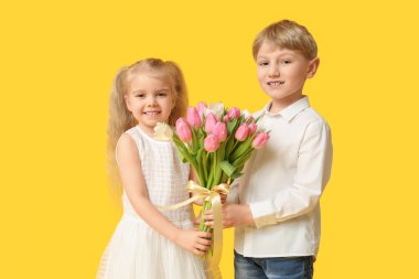 Sarı arka planda bir buket güzel lalesi olan şirin küçük çocuklar. Uluslararası Kadınlar Günü
