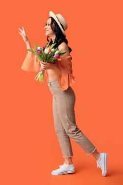 Turuncu arka planda bir buket lale ile güzel bir genç kadın. Uluslararası Kadınlar Günü