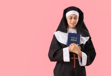 Pembe arka planda İncil 'i olan genç rahibe.