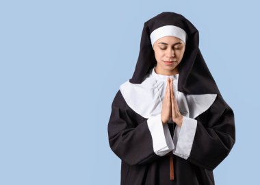 Praying young nun on blue background clipart