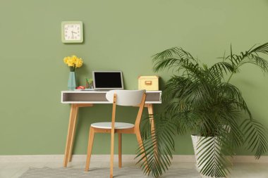 Yeşil duvarda işyeri, ev bitkisi ve saati olan şık bir ofis.