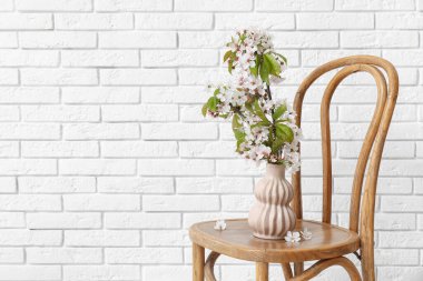 Odadaki beyaz tuğla duvarın yanındaki sandalyede çiçek açan dalları olan vazo.