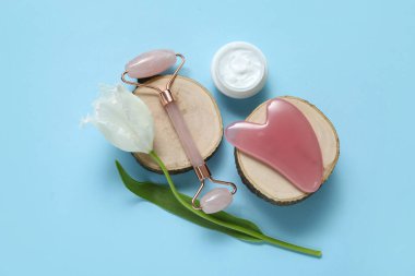 Mavi arka planda gua sha, kozmetik krem ve lale çiçeği ile Jade roller