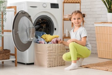Kirli çamaşırları evdeki çamaşır makinesine koyan küçük kız.