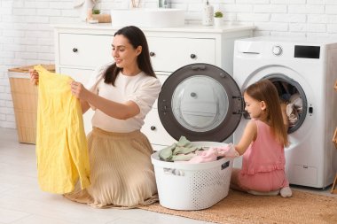 Genç kadın ve kızı evde yıkanmış çamaşırları kontrol ediyorlar.