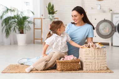 Gülümseyen anne ve kız evde temiz çamaşırlarla yerde oturuyorlar.