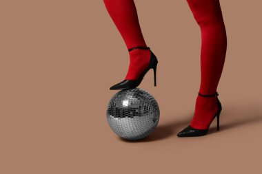 Kahverengi arka planda disko topu olan şık kırmızı taytlı genç bir kadının bacakları.