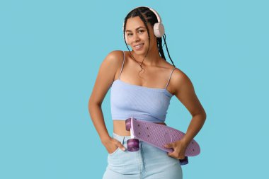 Kaykaylı genç Afro-Amerikalı kadın mavi arka planda müzik dinliyor.