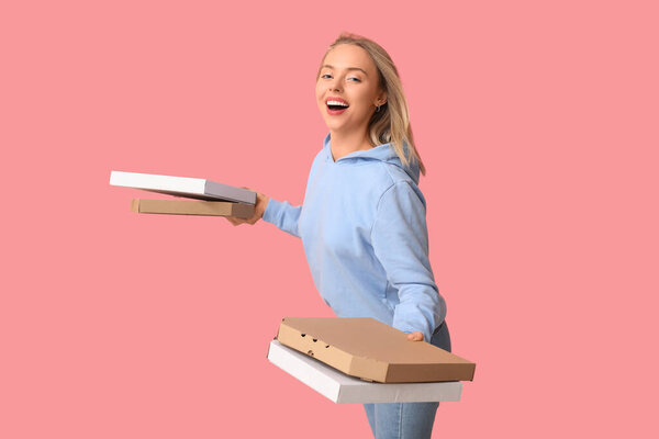 Молодая женщина держит картонные коробки с вкусной пиццей на розовом фоне