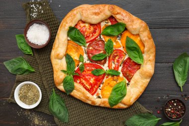 Lezzetli domates galetesi, taze fesleğen ve koyu arkaplanda baharatlar.