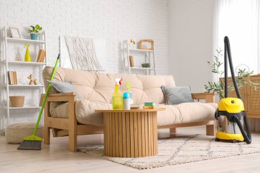 Oturma odasının içinde kanepe, masa ve temizlik malzemeleri var.