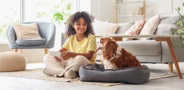 Evde tablet bilgisayarı ve sevimli köpeği olan Afro-Amerikalı bir genç kız.