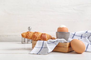 Haşlanmış tavuk yumurtası ve beyaz ahşap arka planda kruvasan.
