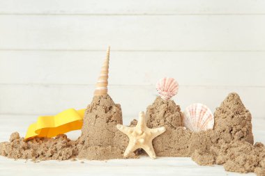 Kumsal oyuncağı, deniz yıldızı ve beyaz ahşap arka planda deniz kabuklarından yapılmış bir kale.