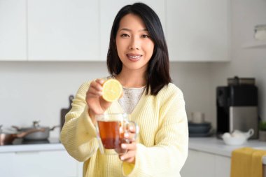 Mutfakta bir fincan lezzetli çay ve limonlu güzel Asyalı kadın.