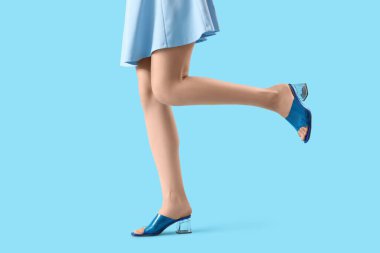 Renkli arka planda mavi sandaletli genç bir kadının bacakları