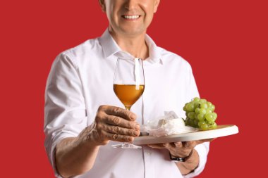 Kırmızı arka planda şarap ve atıştırmalıklarla dolu olgun bir adam, yakın plan.