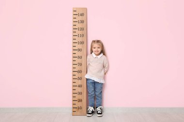 Pembe duvarın yanında boyunu ölçen sevimli küçük bir kız.