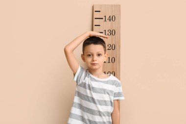 Bej arka planda boy ölçümü yapan sevimli küçük bir çocuk.