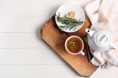Beyaz ahşap masada, içinde kahve ve biberiye çayı olan bir pansiyon.