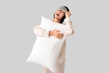 Pijamalı, uyku maskeli, gri arka planda yumuşak yastıklı güzel bir kadın.