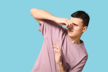 Handsome young man pinching nose because of bad smell on blue background clipart