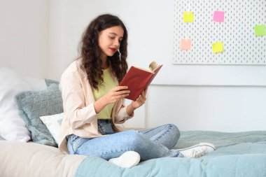 Genç kız yatak odasında kitap okuyor.