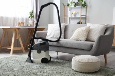 Evdeki gri kanepenin yanındaki halıda modern elektrikli süpürge.