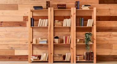 Odasında ahşap duvarın yanında kitapları olan raf ünitesi.