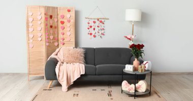 Sevgililer Günü kutlamaları için dekore edilmiş oturma odasının içi katlanır perde, kanepe ve kağıt kalplerle dolu.