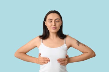 Mavi arka planda göğüslerini kontrol eden genç bir kadın. Kanser farkındalığı kavramı